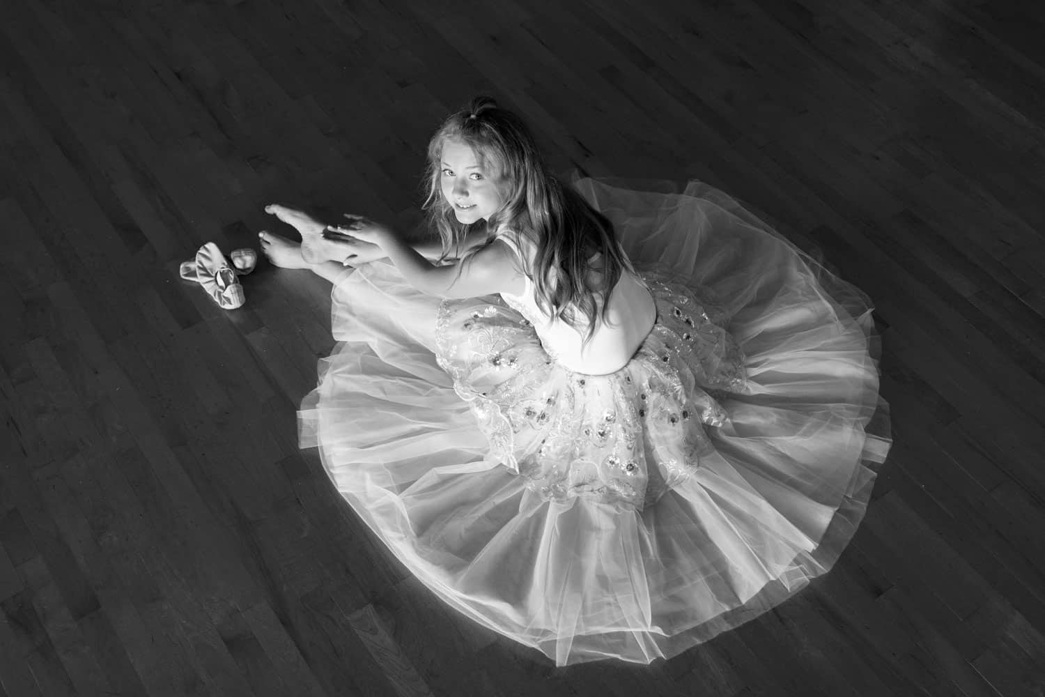 Black and white picture of a ballerina in a white tutu posing on a dance floor.