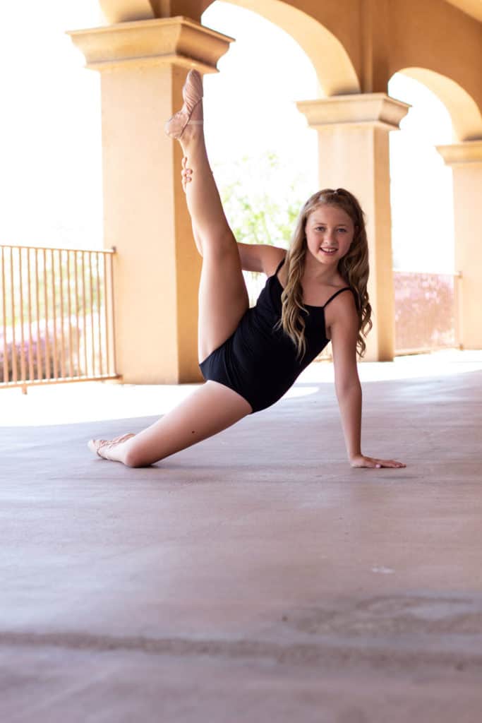 Dancer doing a leg hold on a patio with columns.