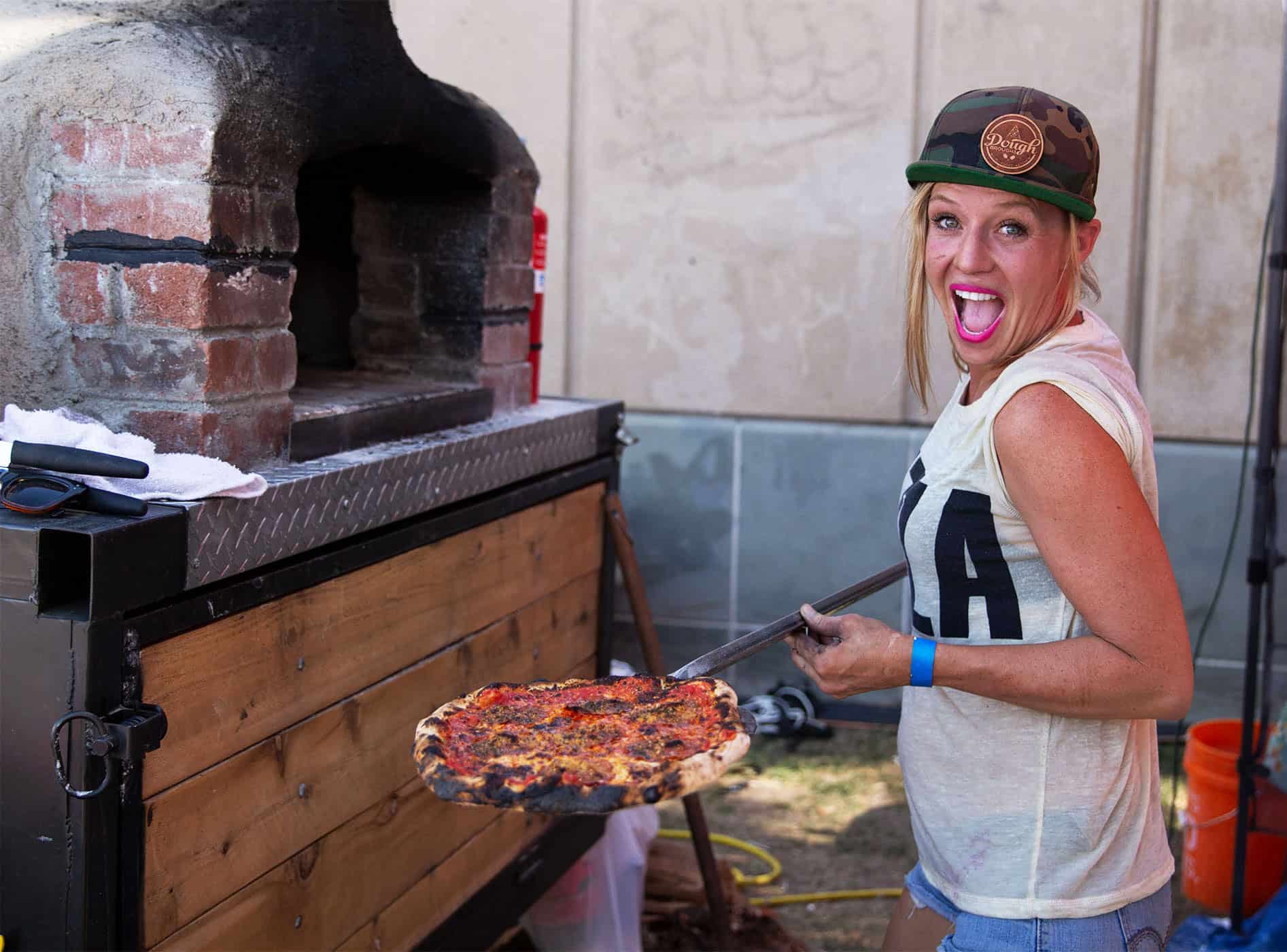 Lady placing a homemade pizza from Dough Broughs Pizza into a red brick oven at a food event in Scottsdale, Arizona.