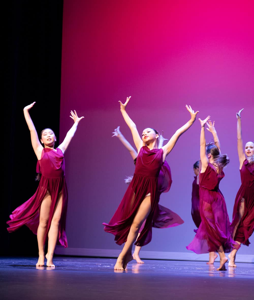 Lyrical dance group performing on stage in maroon dresses in a dance competition.