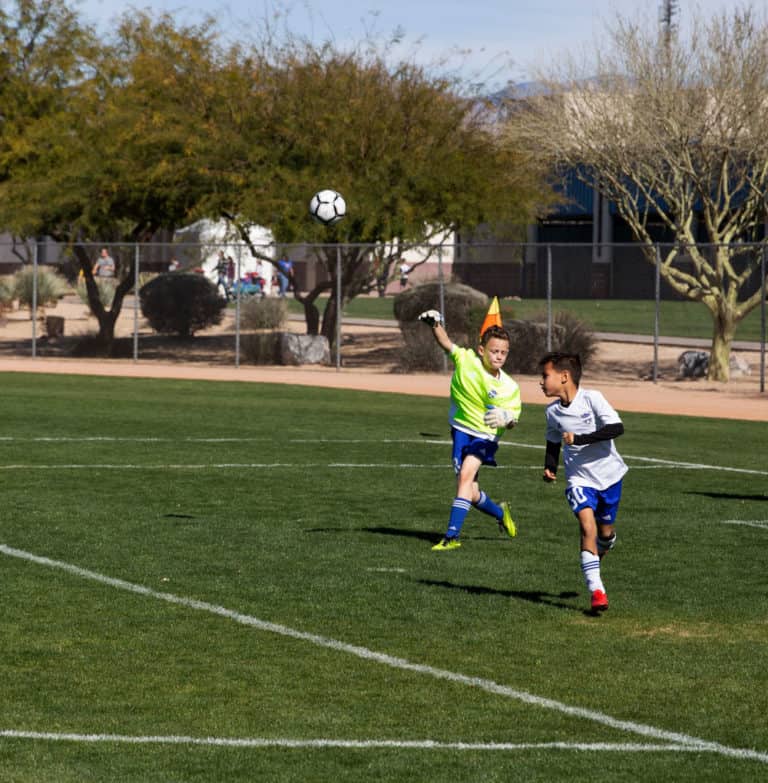 Soccer goalie throwing a soccer ball out of goal in a soccer tournament game.