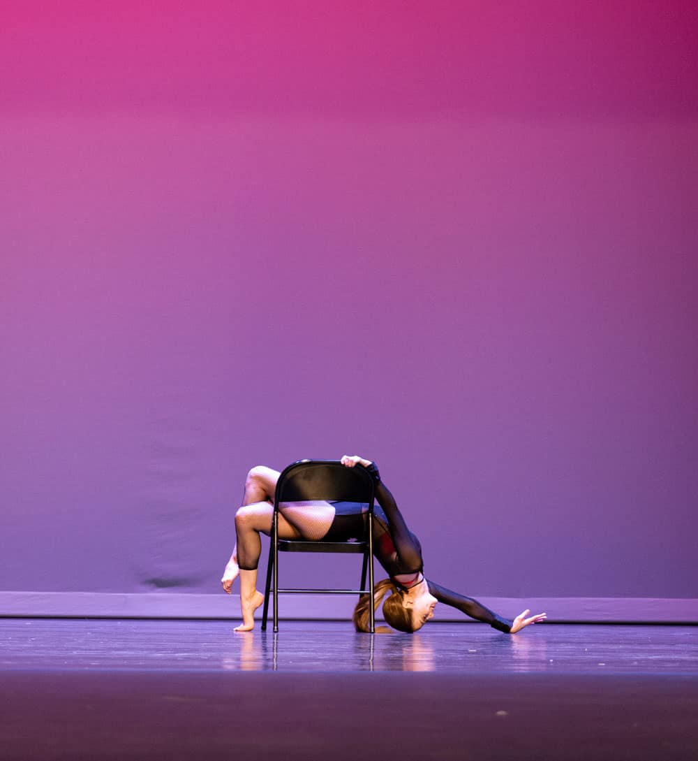 Solo lyrical dancer doing a backbend pose over a chair onstage.